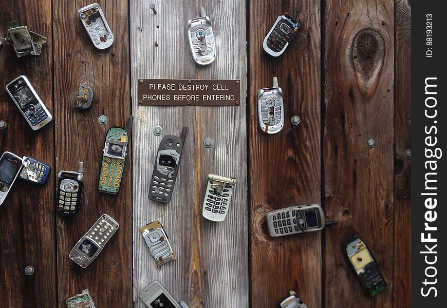 Old damaged cell phones with sign reading please destroy cell phones before entering on rustic wooden boards.