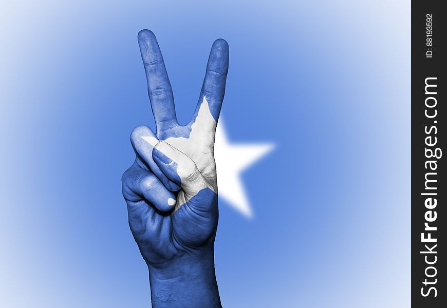 A hand doing the V sign in front of a flag with white star. A hand doing the V sign in front of a flag with white star.
