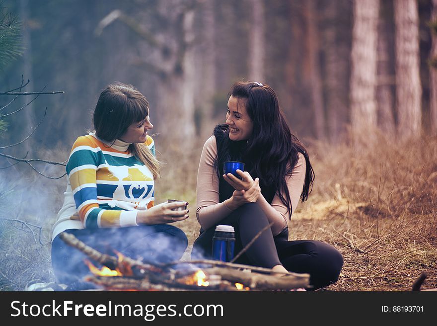 A pair of women sitting at a campfire in the forest. A pair of women sitting at a campfire in the forest.
