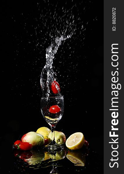 Blank background, red tomatos falling into water in a goblet, peach, tomatoes, lemon on the desk, with their reflection. Blank background, red tomatos falling into water in a goblet, peach, tomatoes, lemon on the desk, with their reflection