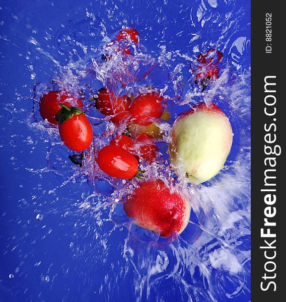 Red tomato, green and white peach,  faling into water over blue background. Red tomato, green and white peach,  faling into water over blue background.