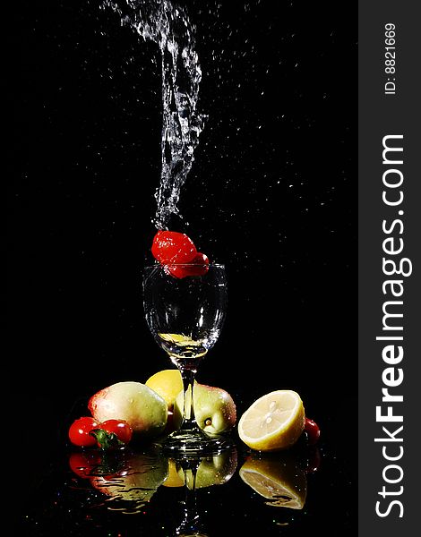 Blank background, red tomatos falling into water in a goblet, peach, tomatoes, lemon on the desk, with their reflection. Blank background, red tomatos falling into water in a goblet, peach, tomatoes, lemon on the desk, with their reflection