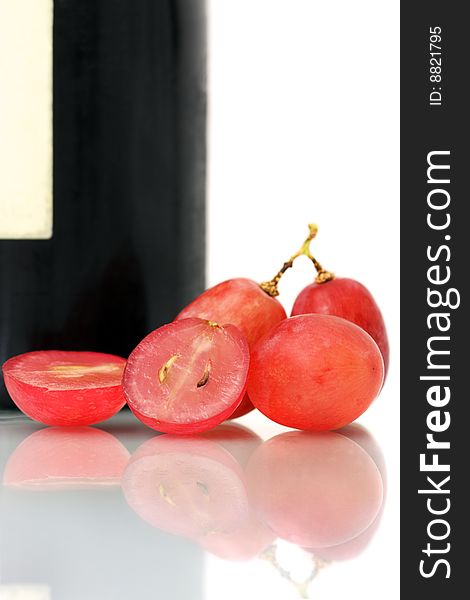 Bunch of red grapes on white plate beside wine bottle. Bunch of red grapes on white plate beside wine bottle.