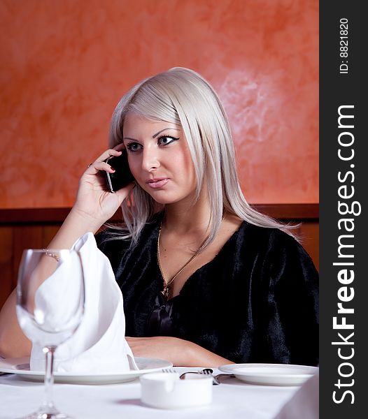 Charming blond girl talking on the phone at the table in a restaurant