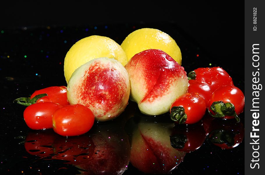 Lemon,s peachs and tomatoes on black background with reflection, yellow, red and green color. Lemon,s peachs and tomatoes on black background with reflection, yellow, red and green color