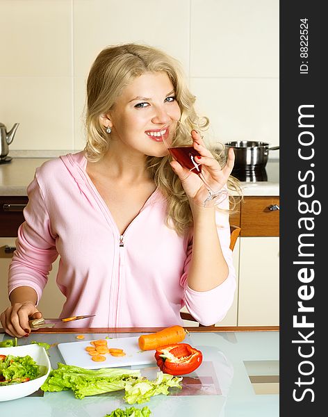 Beautiful young blond woman at home in the kitchen making salad and drinking juice. Beautiful young blond woman at home in the kitchen making salad and drinking juice