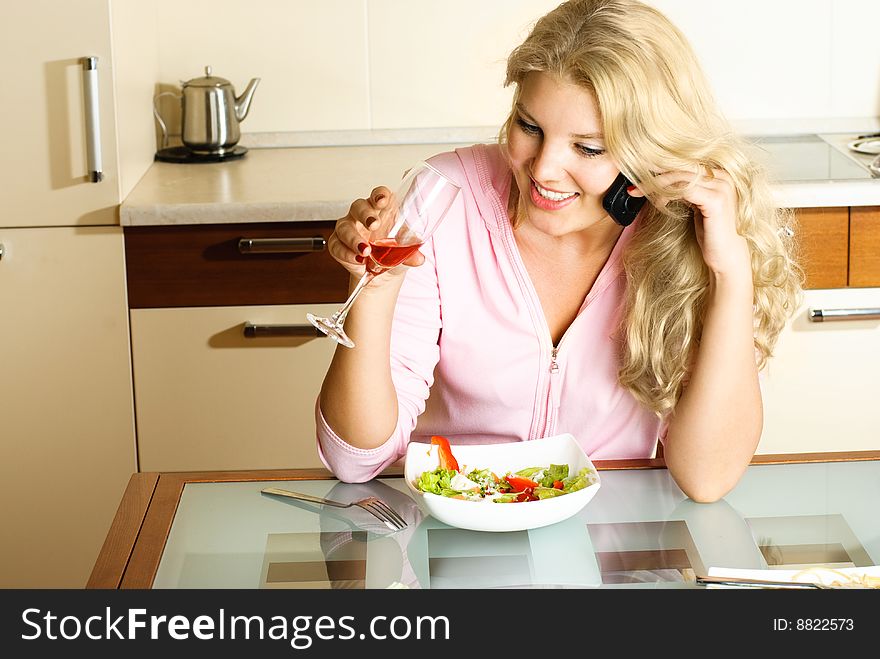 Beautiful blond girl at home in the kitchen eating salad and taking on the cellphone. Beautiful blond girl at home in the kitchen eating salad and taking on the cellphone