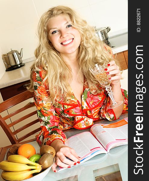 Beautiful happy blond girl at home in the kitchen drinking wine and reading a magazine. Beautiful happy blond girl at home in the kitchen drinking wine and reading a magazine