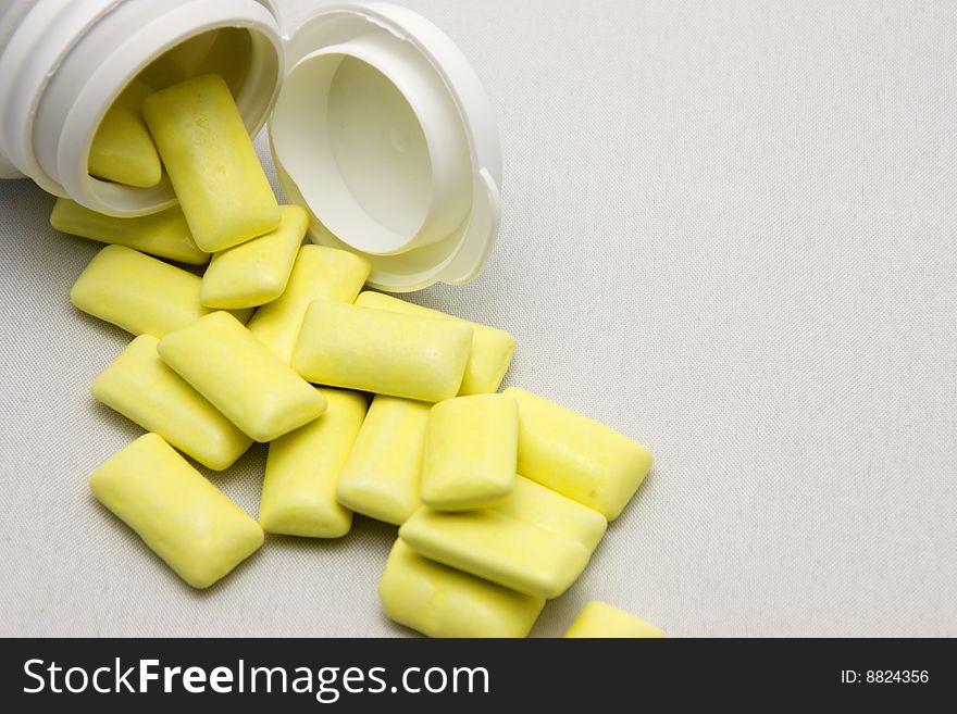 Yellow pills out of container with light background