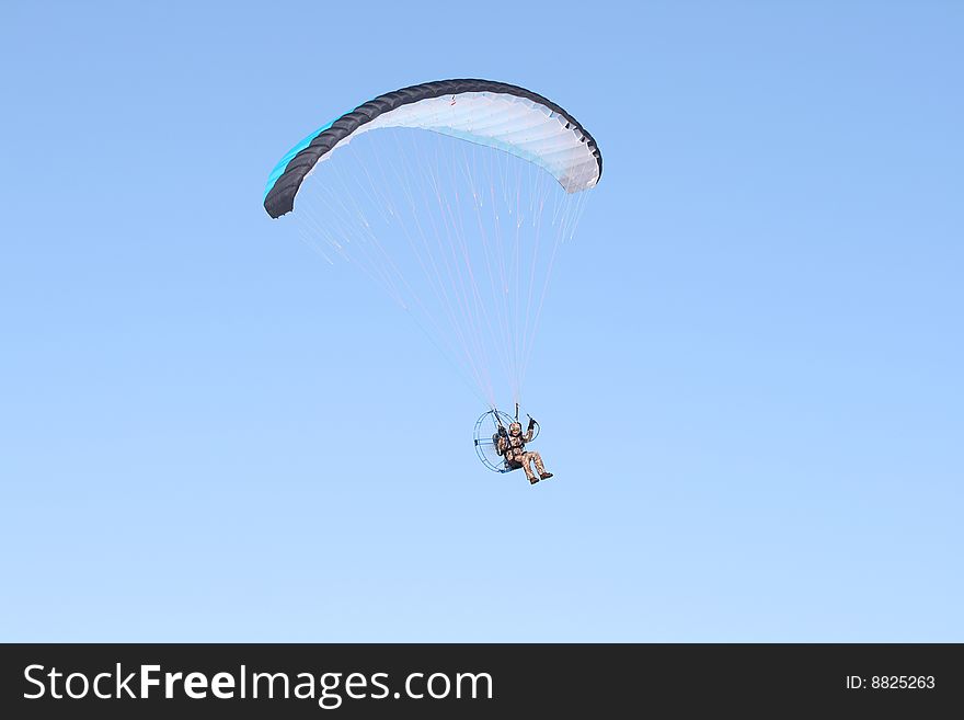 A multi-colored parachute holds up this paraplane on a clear blue day.