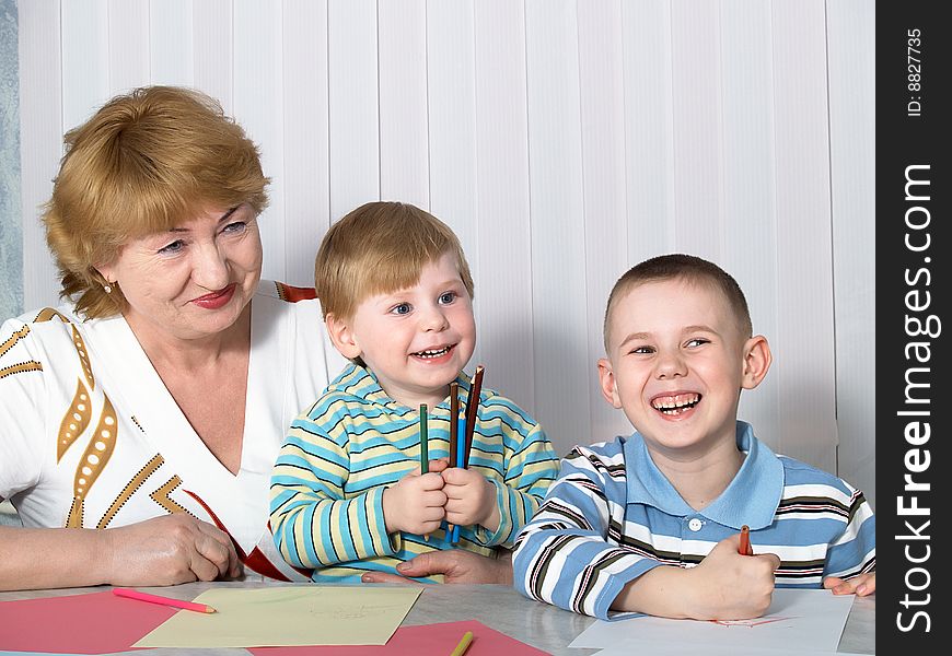 The grandmother is engaged in drawing with two grandsons. The grandmother is engaged in drawing with two grandsons
