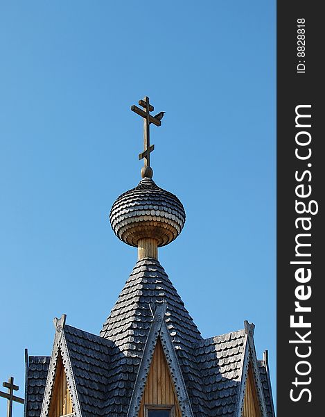 Wooden chapel roof with crow on the cross at sunny spring noon with blue sky. Wooden chapel roof with crow on the cross at sunny spring noon with blue sky