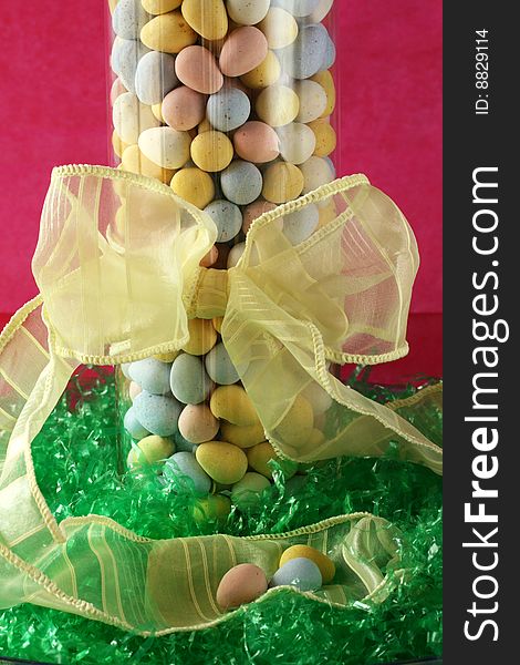 Glass vase full of candy Easter eggs sitting on Easter grass with pink background and yellow bow. Glass vase full of candy Easter eggs sitting on Easter grass with pink background and yellow bow