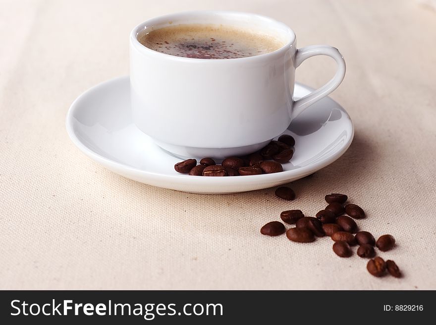 Cup of coffee with coffee beans on the tablecloth