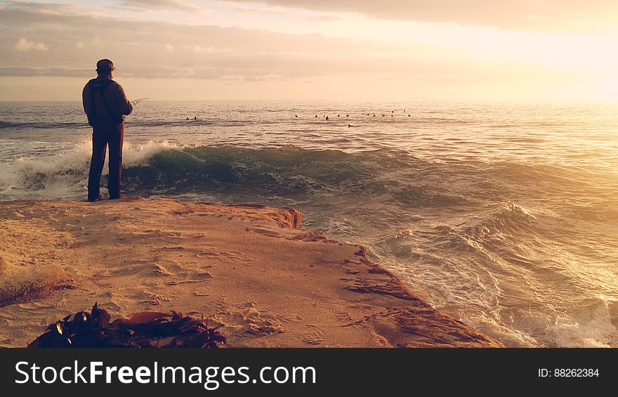 Man Fishing on Sandy Shore by Ocean