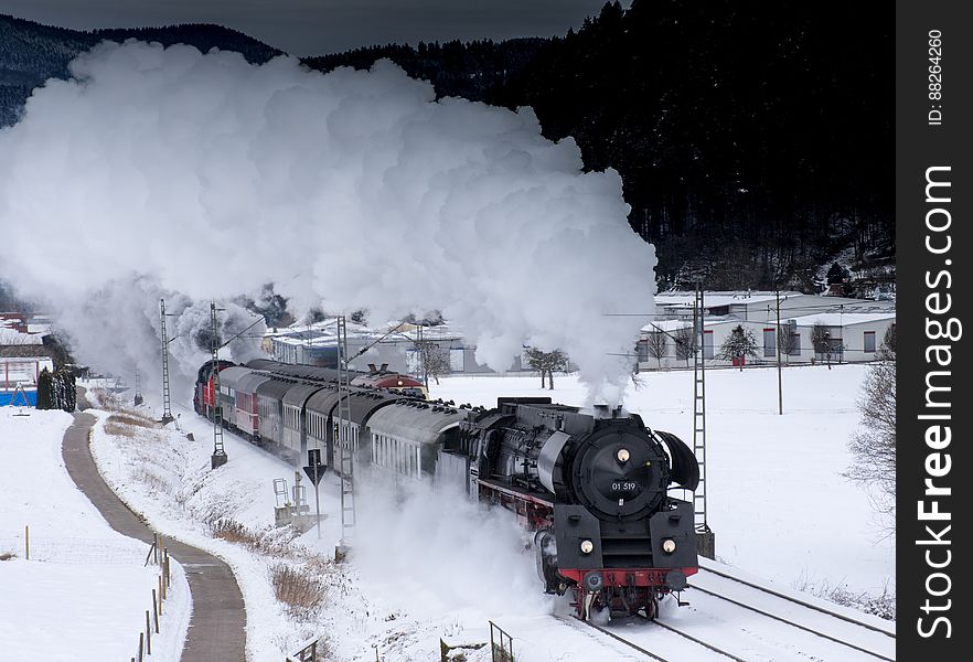 Steam engine pulling train cars on tracks through snow in countryside. Steam engine pulling train cars on tracks through snow in countryside.