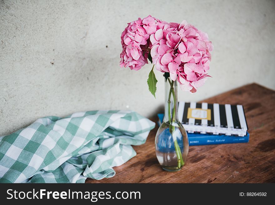 Vase of pink flowers on wooden table with books and checkered material. Vase of pink flowers on wooden table with books and checkered material.