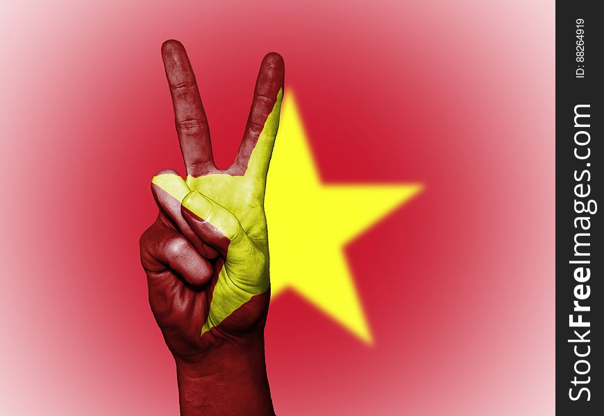A hand doing the V sign in front of a flag with a star. A hand doing the V sign in front of a flag with a star.