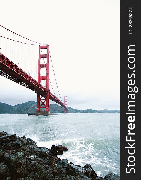 The Golden Gate Bridge and sea waves splashing against the rocky shore, San Francisco, California.