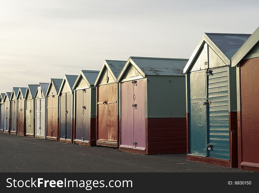 A long row of brightly painted traditional wooden beach huts on the the Sea Front at Brighton in the UK. Warm evening light reflects from the paint. A long row of brightly painted traditional wooden beach huts on the the Sea Front at Brighton in the UK. Warm evening light reflects from the paint