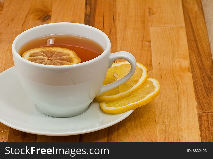 White porcelain cap of tea with sliced lemon on the wooden table. White porcelain cap of tea with sliced lemon on the wooden table