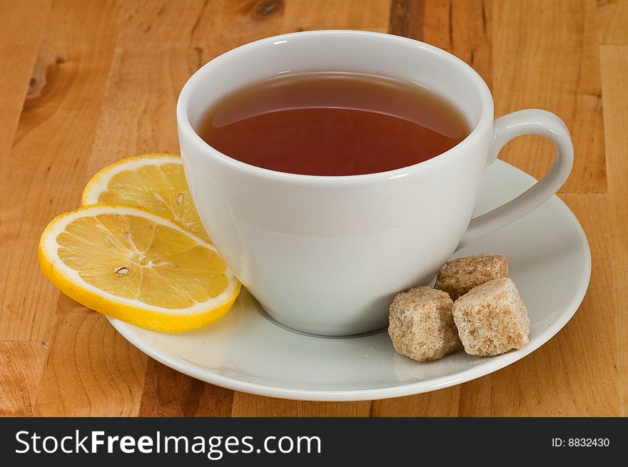 White porcelain cap of tea with sliced lemon and brown sugar on the wooden table. White porcelain cap of tea with sliced lemon and brown sugar on the wooden table