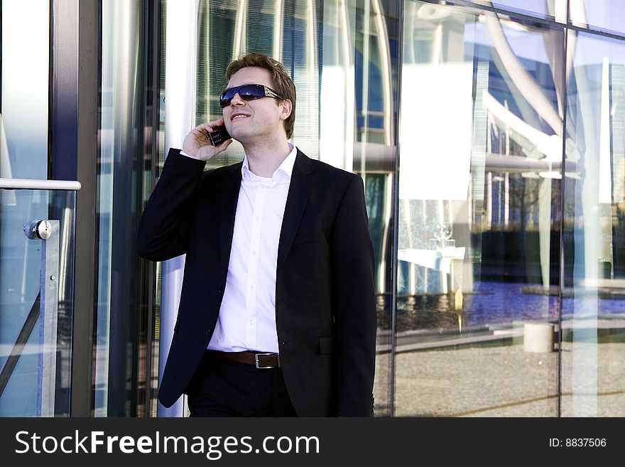 A young executive is speaking on the cell phone outside an office building of glass. A young executive is speaking on the cell phone outside an office building of glass.