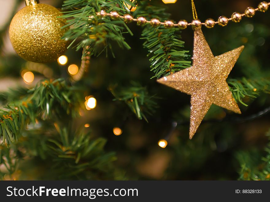 Close up of gold garland, star and ball ornaments on Christmas tree with lights. Close up of gold garland, star and ball ornaments on Christmas tree with lights.