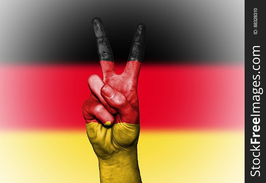 A person doing the V sign with fingers in front of the German Flag. A person doing the V sign with fingers in front of the German Flag.