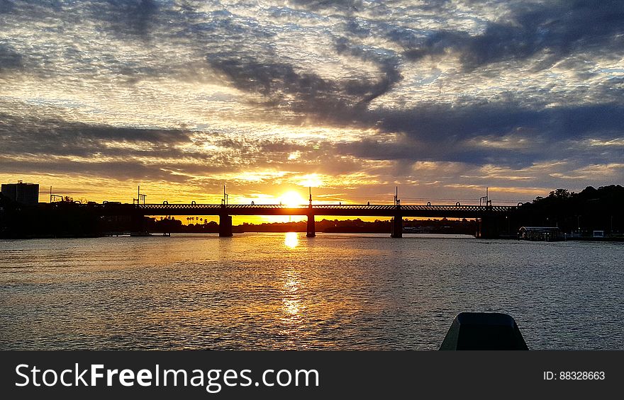 A silhouetted bridge at sunset and sunlight reflecting on the water surface.