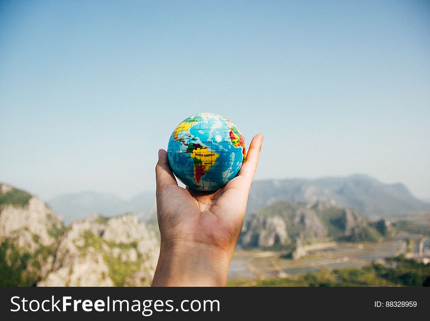 Close up of hand holding globe in scenic landscape.