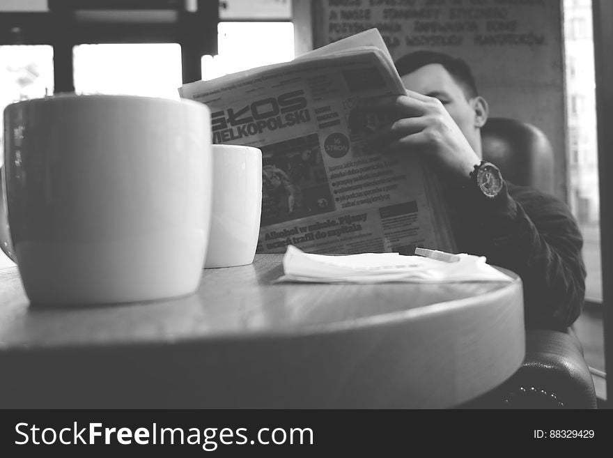 Portrait of man reading newspaper sitting at table in cafe in black and white.