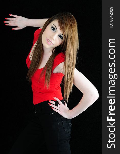 Female fashion model wearing a red top and black jeans with one hand on the black back drop and the other hooked into her jeans belt hole. Female fashion model wearing a red top and black jeans with one hand on the black back drop and the other hooked into her jeans belt hole.