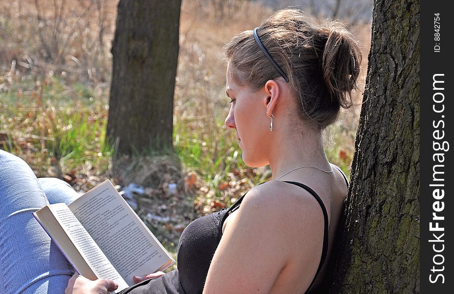 Girl reading a book outdoor, while sitting near the tree