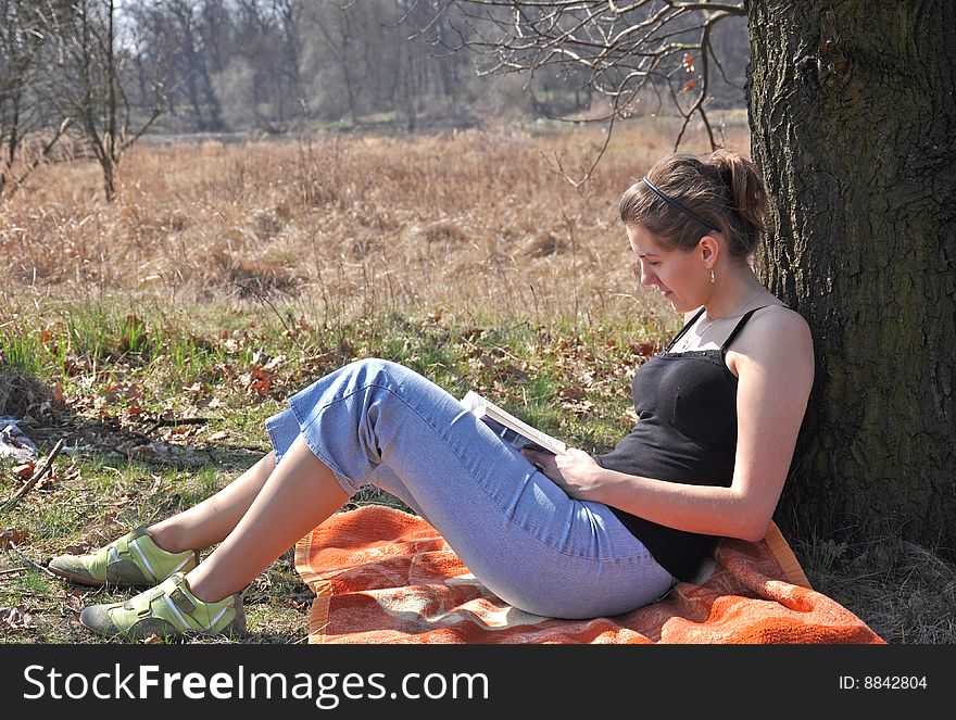 Girl reading a book outdoor, while sitting near the tree