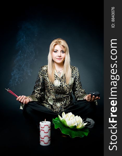 Woman meditating in lotus pose with aroma sticks, lotus, and candle