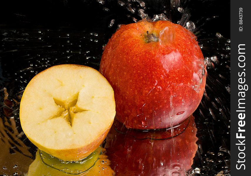 Full apple and half with water splashing on black