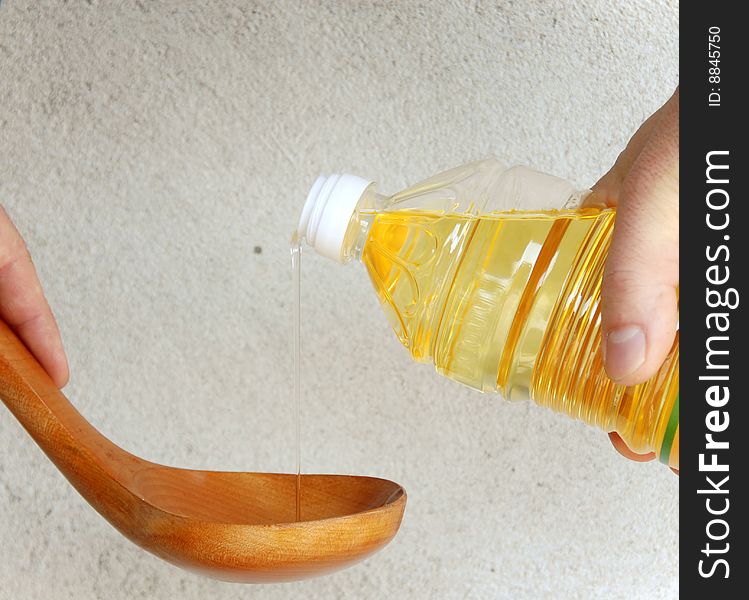 Pouring yellow vegetable oil into wooden spoon over gray background. Pouring yellow vegetable oil into wooden spoon over gray background