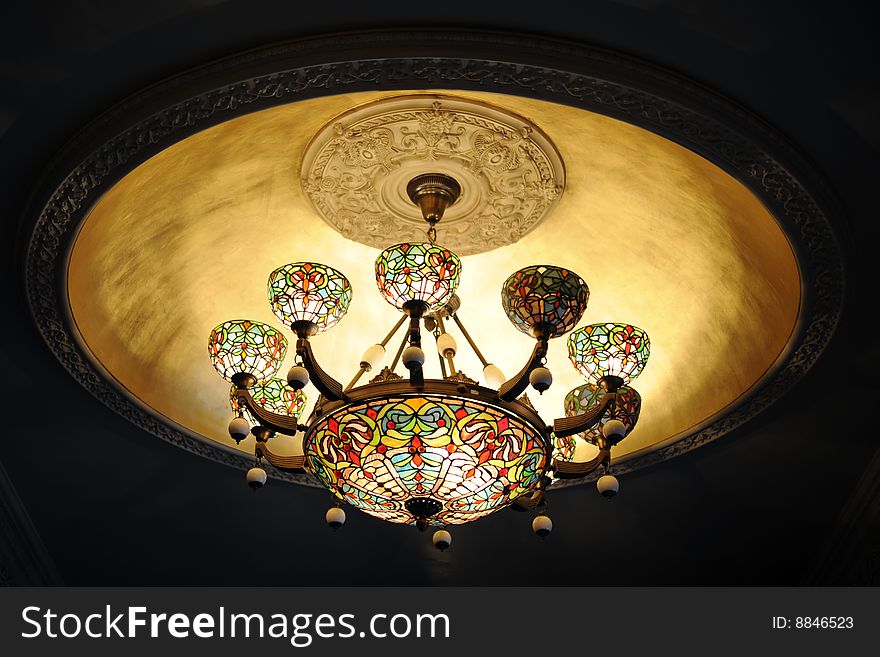 A lit stained glass chandelier against a darkened ceiling. A lit stained glass chandelier against a darkened ceiling.