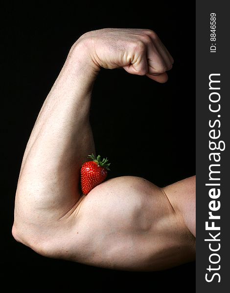 Muscled male arm holds strawberry while flexing his bicep. Muscled male arm holds strawberry while flexing his bicep.