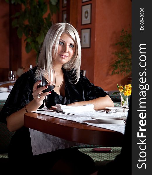 Charming blond girl in a restaurant with a glass of red wine