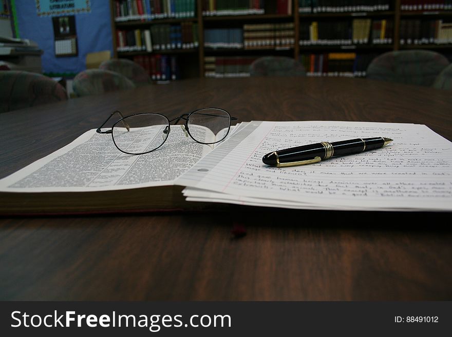 An open book with notes and eyeglasses on a library table. An open book with notes and eyeglasses on a library table.