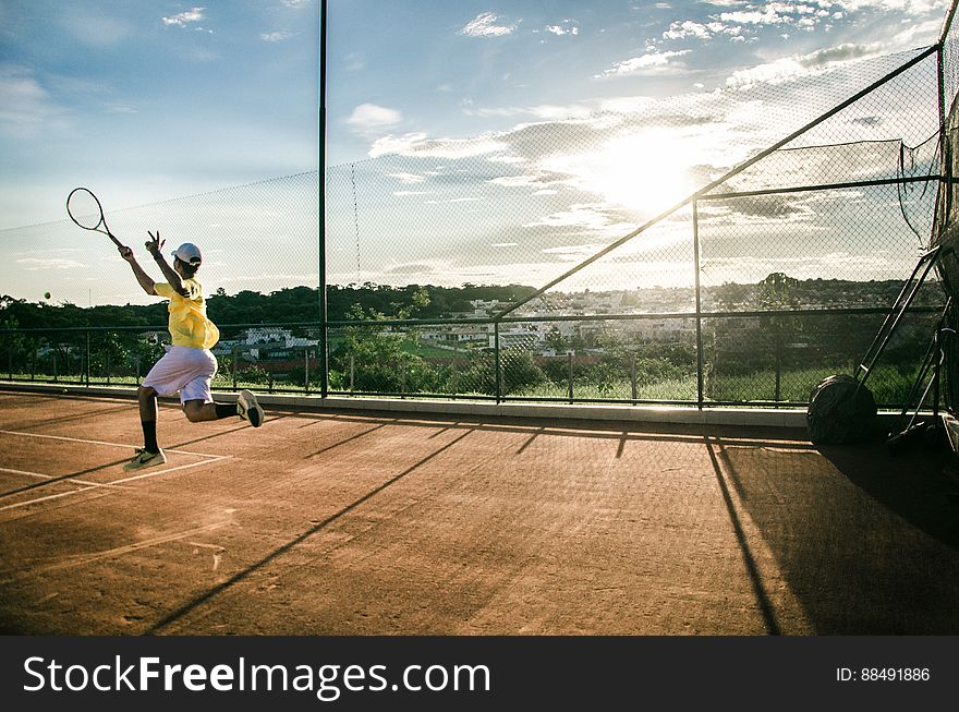 Male tennis player jumping in air on clay court with sun glare. Male tennis player jumping in air on clay court with sun glare.