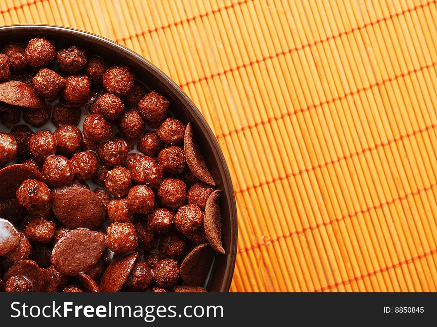 Milk with chocolate cereals in a bowl over orange bamboo mat. Milk with chocolate cereals in a bowl over orange bamboo mat