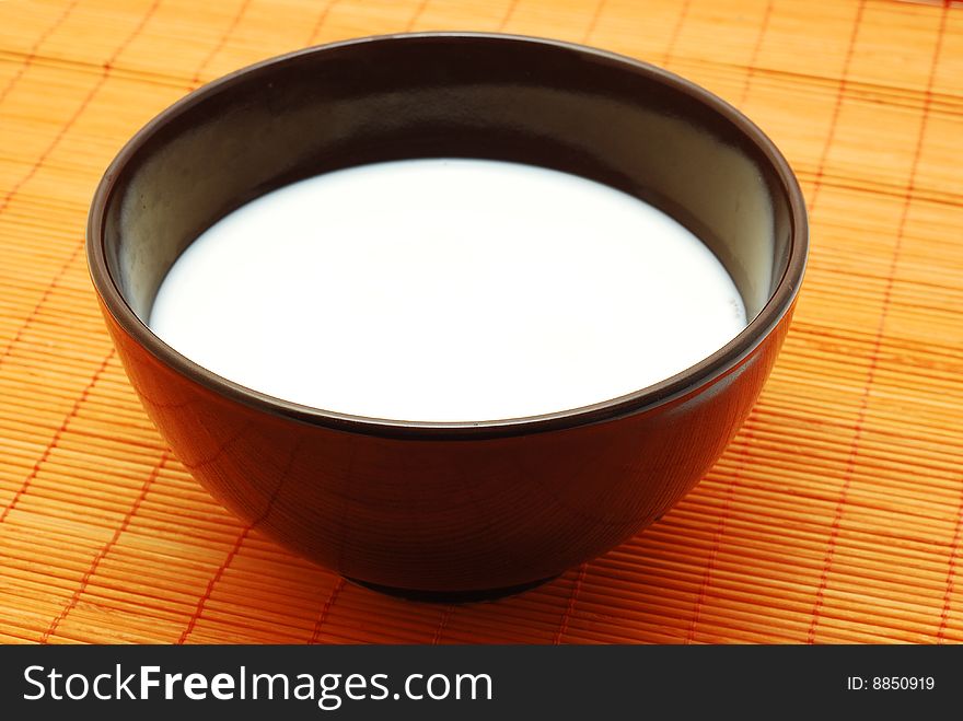 Milk in a bowl over orange bamboo mat