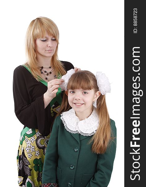 Mother is helping her's young daughter prepare to school. Woman is filleting ribbon on girl's hair. Mom is brushing young schoolgirl's hair. Isolated on white in studio. Mother is helping her's young daughter prepare to school. Woman is filleting ribbon on girl's hair. Mom is brushing young schoolgirl's hair. Isolated on white in studio.