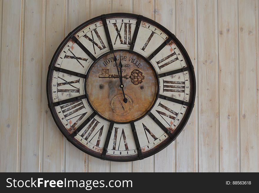 A close up of an old fashioned clock with Roman numerals hanging on a wall.