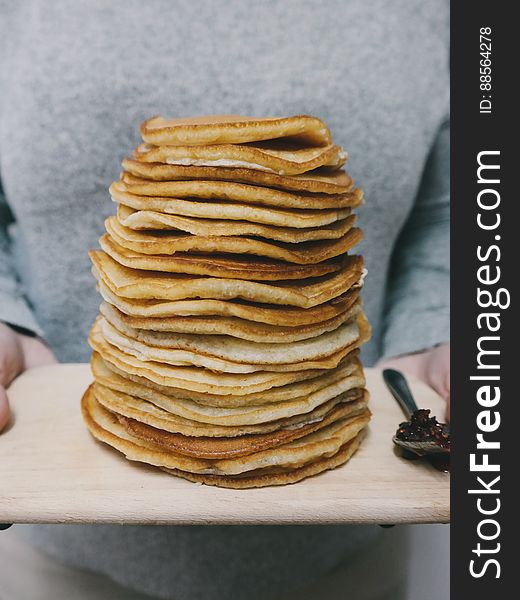 A person holding a wooden tray full of pancakes. A person holding a wooden tray full of pancakes.
