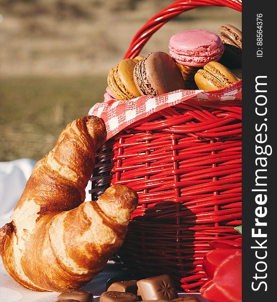 A picnic basket of French macarons and croissants with chocolates on the side. A picnic basket of French macarons and croissants with chocolates on the side.