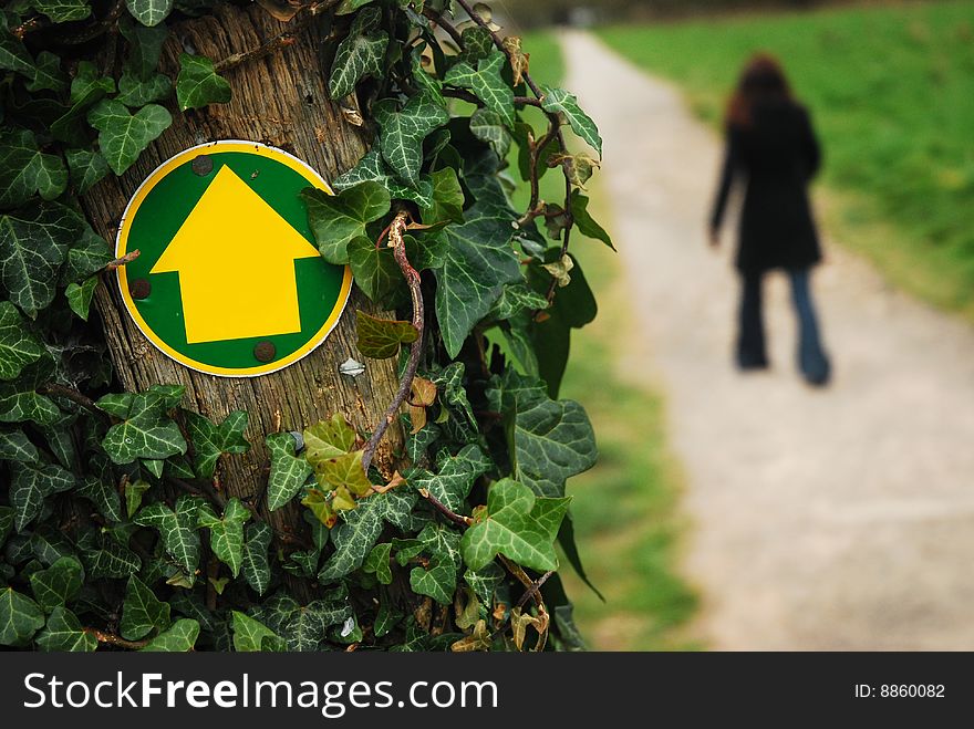 An arrow engulfed in ivy showing onward direction of path with woman walking down. An arrow engulfed in ivy showing onward direction of path with woman walking down.